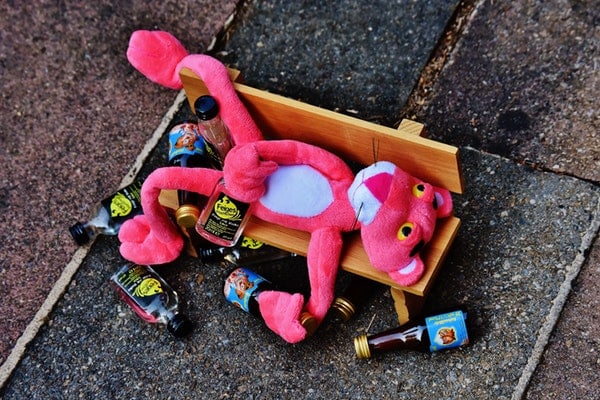 A pink cheetah doll getting drunk with empty bottles on a bench